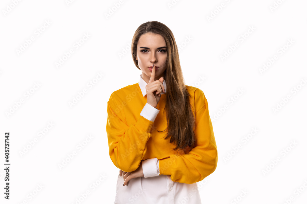 Portrait of young brunette woman keeping finger at her mouth, saying Shh, Hush, Tsss. Studio shot, white background Portrait of young brunette woman keeping finger at her mouth, saying Shh, Hush, Tsss. Studio shot, white background