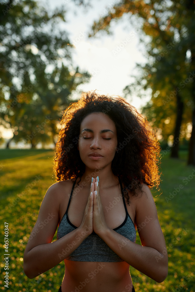 The power of breathing and meditation. Young calm mixed race woman with closed eyes keeping palms together and meditating, practicing yoga outdoors in green park The power of breathing and meditation. Young calm mixed race woman with closed eyes keeping palms together and meditating, practicing yoga outdoors in green park