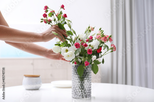 Fototapeta Naklejka Na Ścianę i Meble -  Woman taking beautiful flowers from vase on white table in room, closeup