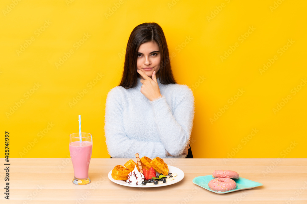 Young woman eating waffles and milkshake in a table over isolated yellow background laughing Young woman eating waffles and milkshake in a table over isolated yellow background laughing