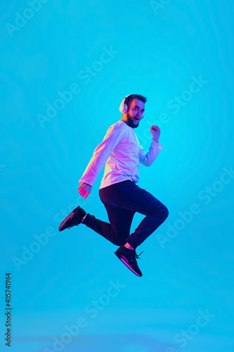 Fototapeta Naklejka Na Ścianę i Meble -  Jumping high. Caucasian man's portrait isolated on blue studio background in neon light. Beautiful male model. Concept of human emotions, facial expression, sales, ad. Copyspace for ad. Flyer