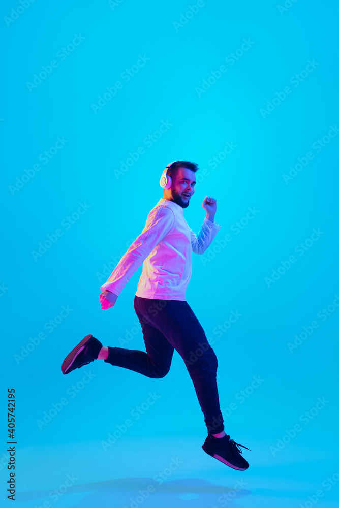 Jumping high. Caucasian man's portrait isolated on blue studio background in neon light. Beautiful male model. Concept of human emotions, facial expression, sales, ad. Copyspace for ad. Flyer