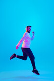 Jumping high. Caucasian man's portrait isolated on blue studio background in neon light. Beautiful male model. Concept of human emotions, facial expression, sales, ad. Copyspace for ad. Flyer