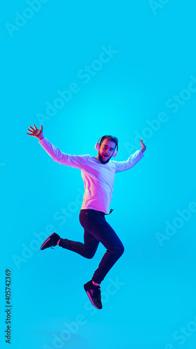 Jumping high. Caucasian man's portrait isolated on blue studio background in neon light. Beautiful male model. Concept of human emotions, facial expression, sales, ad. Copyspace for ad. Flyer © master1305