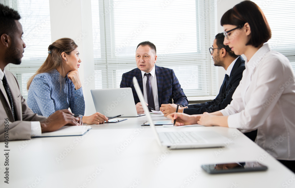 Group of business people sitting around the office desk and discussing the project Group of business people sitting around the office desk and discussing the project