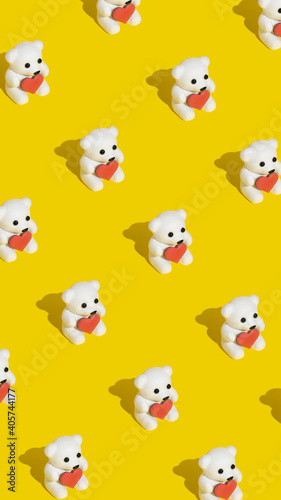 Pattern made with white teddy bears holding a heart shaped cookie on modern trendy yellow background. Minimal Valentines  romantic or love concept. Copy space.
