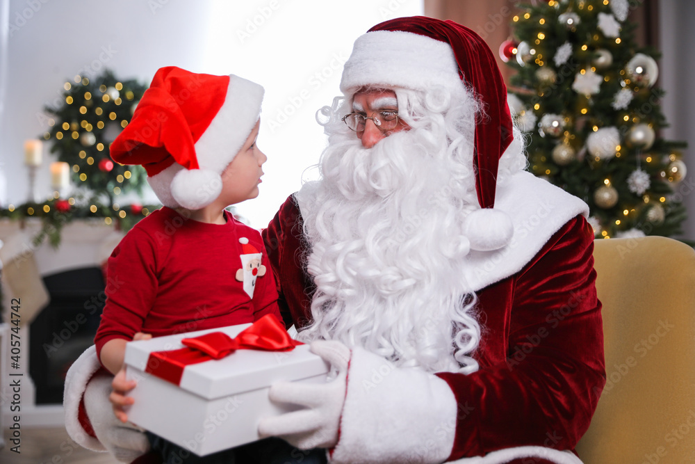 Santa Claus giving present to little boy in room decorated for Christmas Santa Claus giving present to little boy in room decorated for Christmas