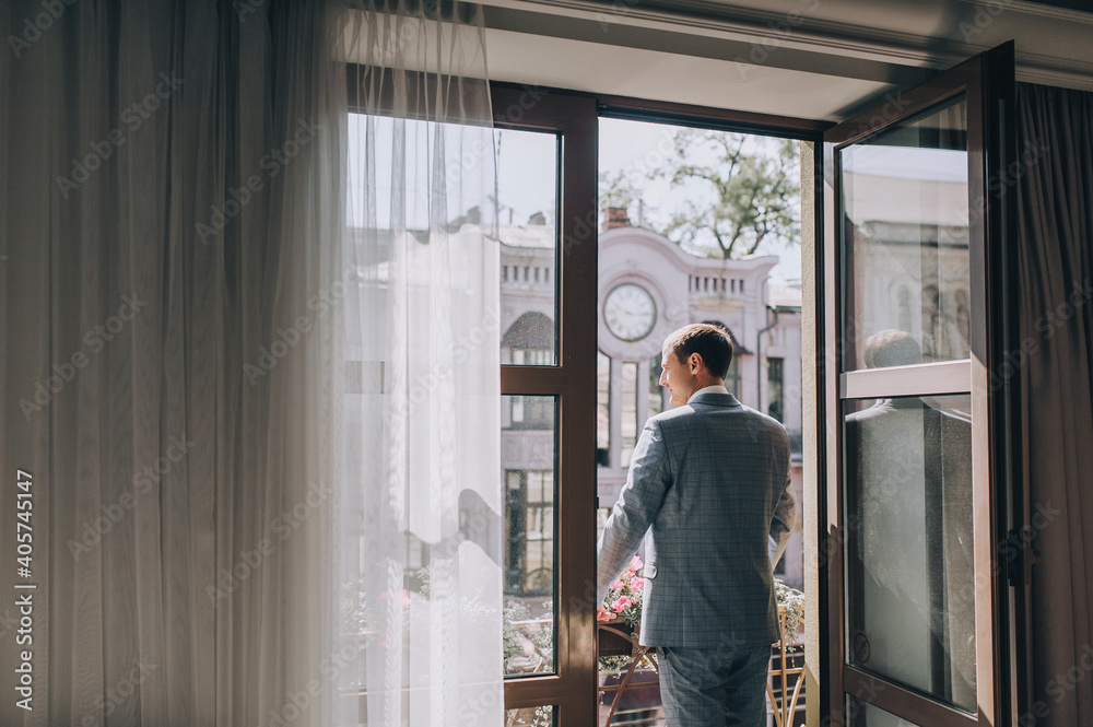 Stylish groom, man, gentleman stands near the window on the terrace, veranda in the hotel against the backdrop of the city on a sunny day. Wedding portrait. Stylish groom, man, gentleman stands near the window on the terrace, veranda in the hotel against the backdrop of the city on a sunny day. Wedding portrait.