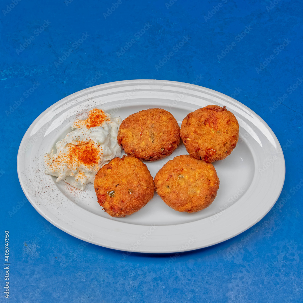 vegan zucchini fried balls with yogurt sauce served in a white dish on blue table surface vegan zucchini fried balls with yogurt sauce served in a white dish on blue table surface