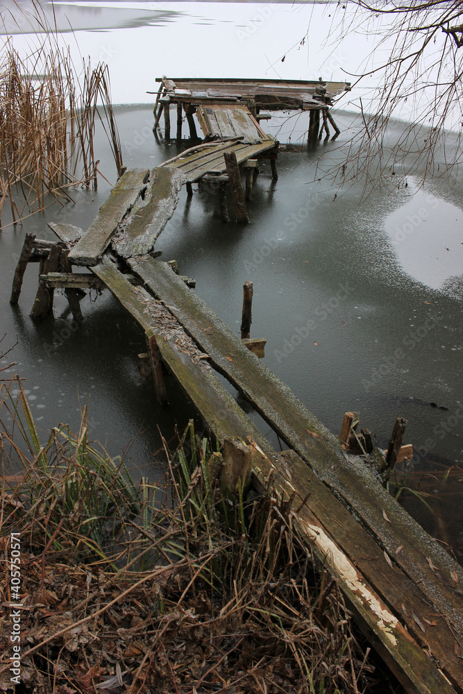 Wooden bridge in the river. Handcrafted fishing bridge on the frozen river among dry reeds. Calm winter landscape