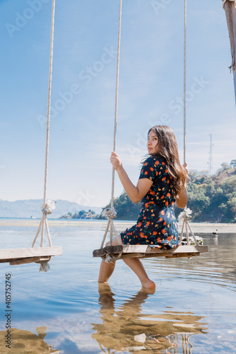Young woman sitting on a swing in the middle of Lake Atitlan - female traveler enjoying Lake Atitlan in Guatemala - lake landscape in the morning