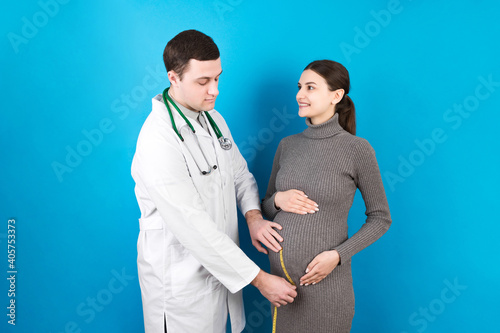 happy beautiful pregnant young woman touching her bare tummy while a doctor is measuring it