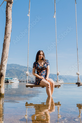 Young woman sitting on a swing in the middle of Lake Atitlan - female traveler enjoying Lake Atitlan in Guatemala - lake landscape in the morning