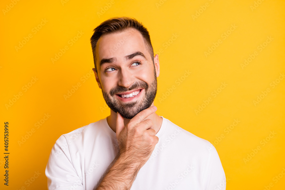 Portrait of optimistic guy look empty space hand chin wear white t-shirt isolated on vibrant yellow color background Portrait of optimistic guy look empty space hand chin wear white t-shirt isolated on vibrant yellow color background