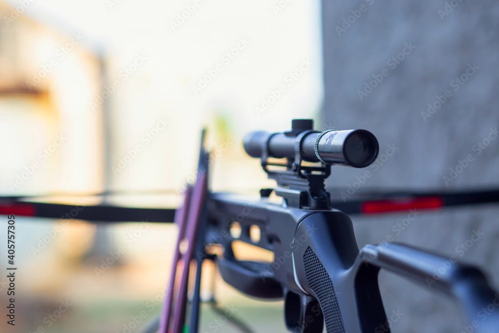 A modern crossbow with arrows and a telescopic sight lies on a wooden table in the street. Preparing for the hunt.