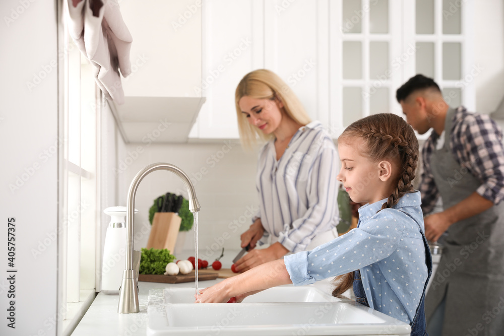 Little girl washing vegetables and her parents in modern kitchen Little girl washing vegetables and her parents in modern kitchen