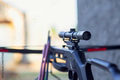 A modern crossbow with arrows and a telescopic sight lies on a wooden table in the street Fototapeta
