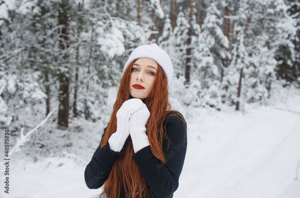 Young red-haired girl with long red hair on a winter background.Red-haired woman in a white hat on the background of winter nature. Young red-haired girl with long red hair on a winter background.Red-haired woman in a white hat on the background of winter nature.