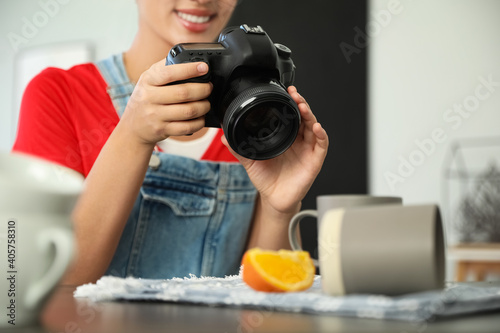 Young photographer taking picture of cups at table indoors, closeup