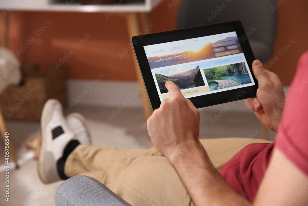 Man with tablet booking tickets online at home, closeup. Travel agency concept