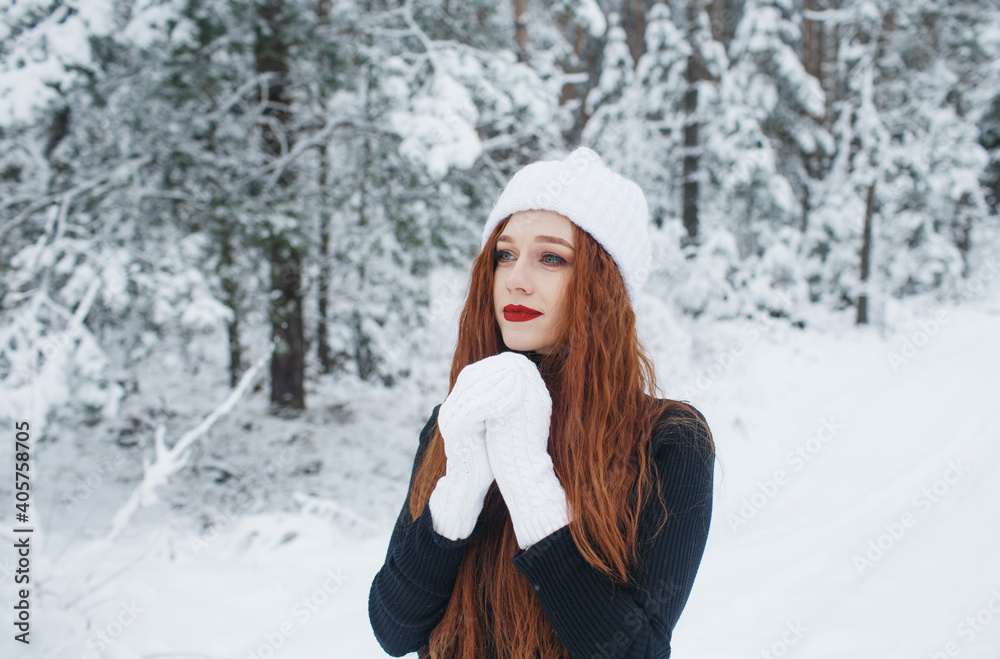 Young red-haired girl with long red hair on a winter background.Red-haired woman in a white hat on the background of winter nature. Young red-haired girl with long red hair on a winter background.Red-haired woman in a white hat on the background of winter nature.
