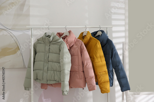 Different warm jackets hanging on rack indoors photo