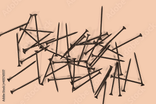 A bunch of self-tapping screws for wood surfaces on a beige background. Metal fasteners. © ss404045