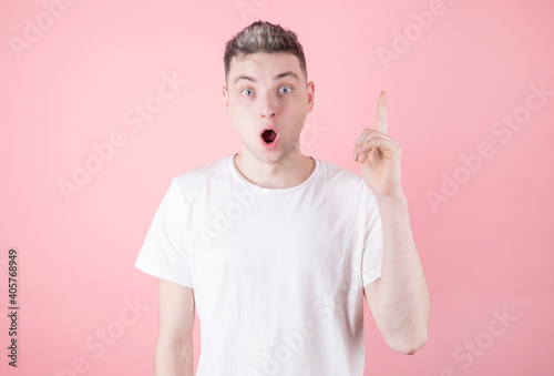 Close up portrait of charming young man pointing with finger while looking at camera isolated on pink background