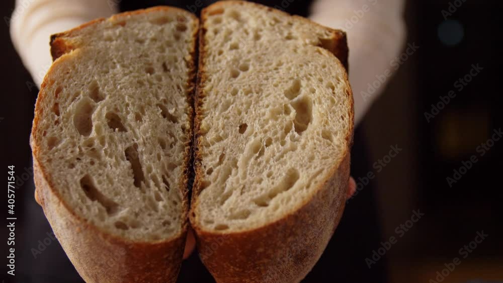 food cooking, baking and people concept - female baker showing loaf of bread cut in two halves at bakery or kitchen