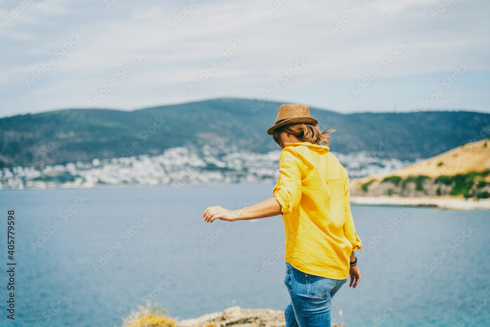 young woman in a yellow shirt and hat enjoying sea view, summer vacation and travel.