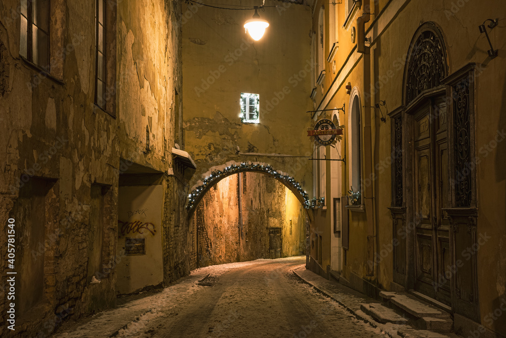 Beautiful narrow street of Vilnius Old Town, evening or night view with old buildings and street lamp in winter with snow