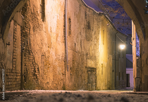 Beautiful narrow street of Vilnius Old Town, evening or night view with old buildings and street lamp in winter with snow