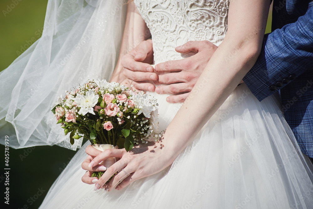 the groom embraces the bride. hands of the bride with a bouquet of pink and white flowers. tenderness, wedding. the groom embraces the bride. hands of the bride with a bouquet of pink and white flowers. tenderness, wedding.