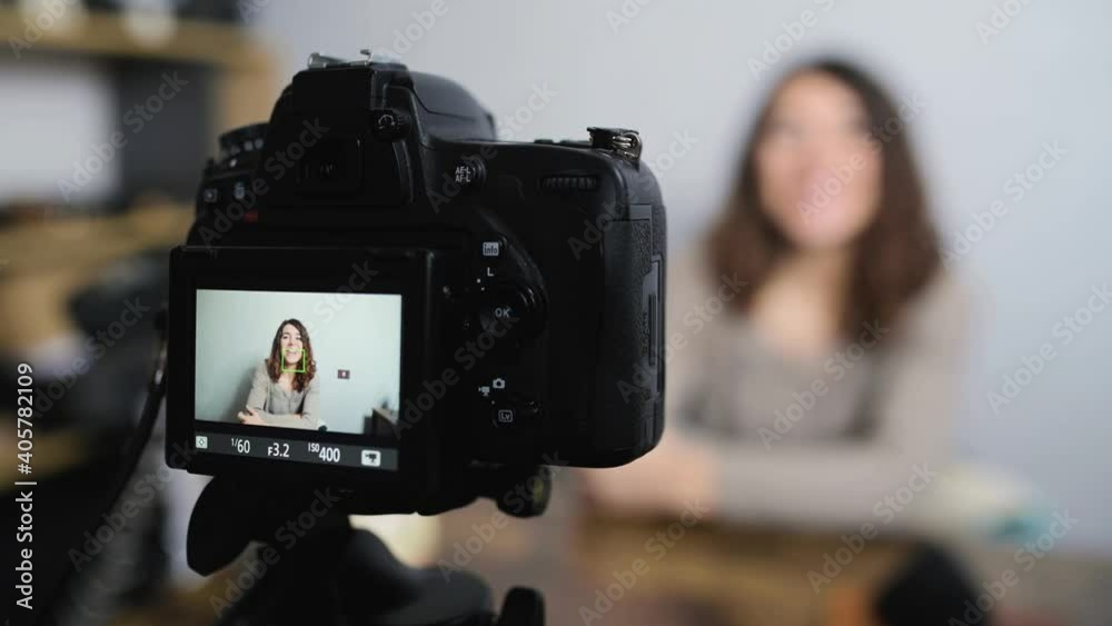 Young smiling woman sitting at the desk talking to the camera while taking a shot. Vlog and freelancer concept. Young smiling woman sitting at the desk talking to the camera while taking a shot. Vlog and freelancer concept.