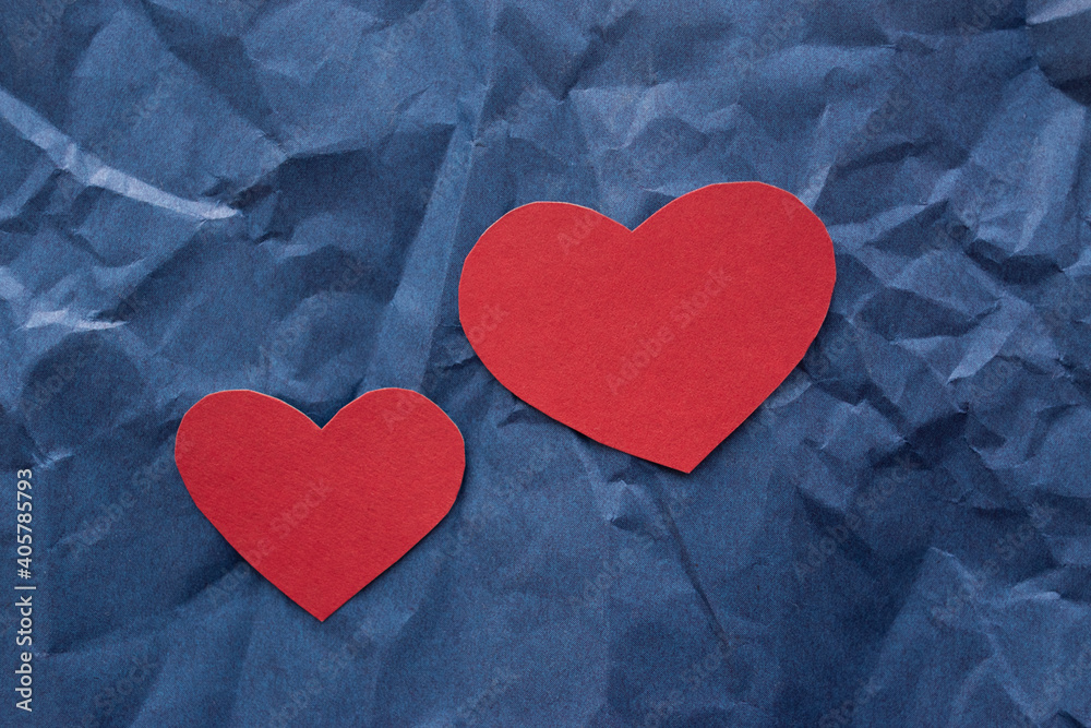 Obraz premium Two hearts made of red cardboard, one small, the other large, lie on a blue background of crumpled paper