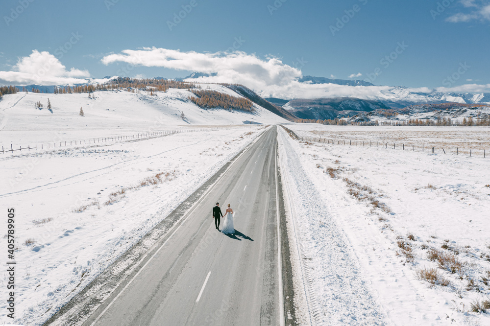 Bride and groom in a dress on a snowy road among the mountains in autumn in Altai Bride and groom in a dress on a snowy road among the mountains in autumn in Altai