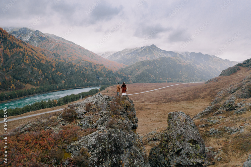The bride and groom stand on the top of a rock against the background of mountains in autumn in Altai