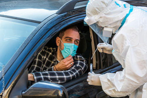 Man sitting in car, waiting for medical worker in PPE to perform drive-thru COVID-19 test © MexChriss