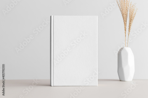 White book mockup with a dried grass in a vase on the beige table.