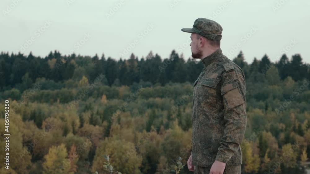 Handsome soldier in camouflage uniform observe territory from a hill. Young army force member in the forest Handsome soldier in camouflage uniform observe territory from a hill. Young army force member in the forest