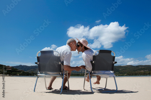coppia di anziani si tiene teneramente la mano seduti in una sedia in spiaggia