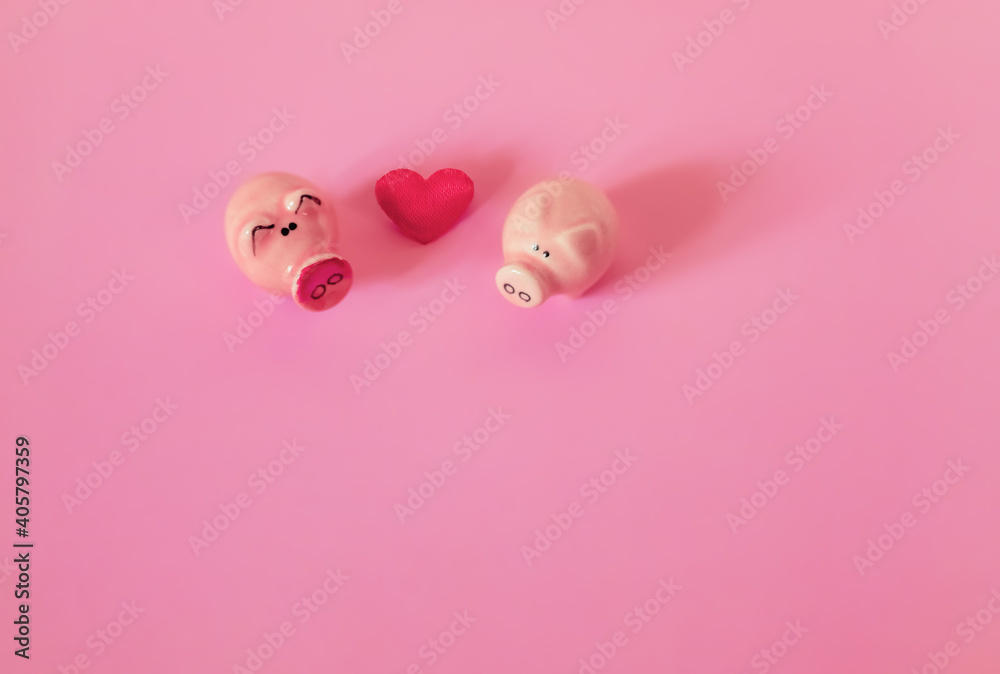 Two figurines of pigs and a heart on a pink background. Composition for Valentine's Day. Flat lay, copy space, top view.