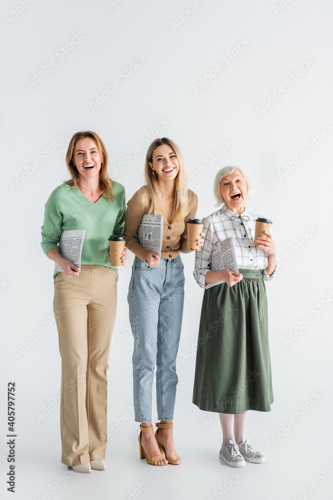 full length of three generation of cheerful women holding newspapers and paper cups on white full length of three generation of cheerful women holding newspapers and paper cups on white