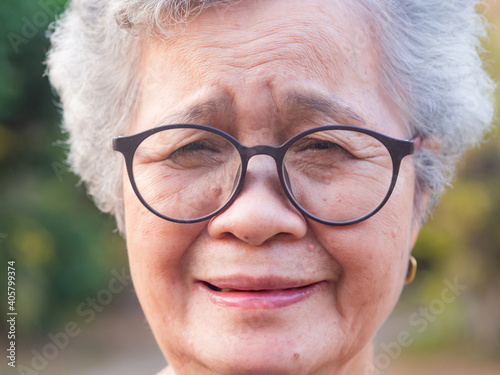 Close-up of face elderly Asian woman wearing glasses smile and looking at the camera while standing a garden. Concept of aged people and healthcare
