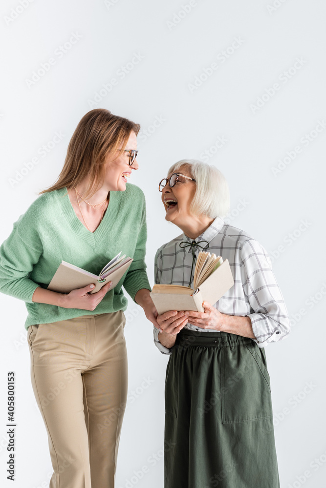 senior mother laughing with daughter in glasses while holding books isolated on white senior mother laughing with daughter in glasses while holding books isolated on white