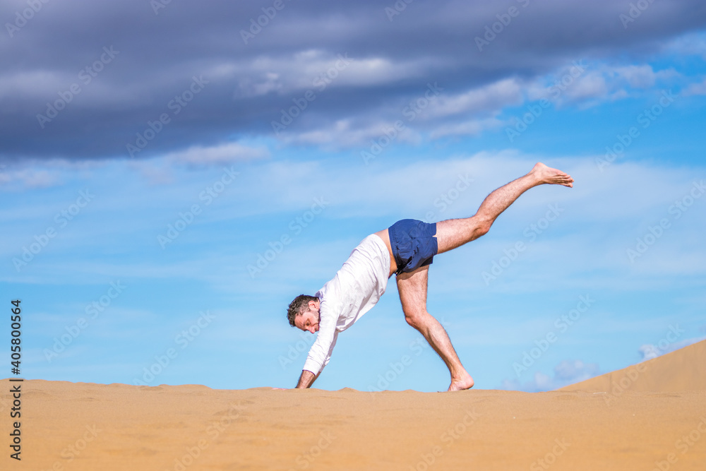 Young athletic man doing acrobatics in the sand of the dunes in Gran Canaria Young athletic man doing acrobatics in the sand of the dunes in Gran Canaria