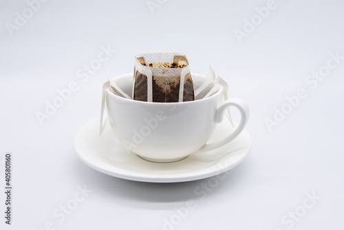 Drip or brewed coffee in white cup on white backdrop. Paper dripping bag on a cup