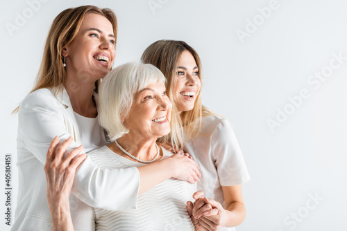 three generation of positive women smiling while hugging isolated on white photo