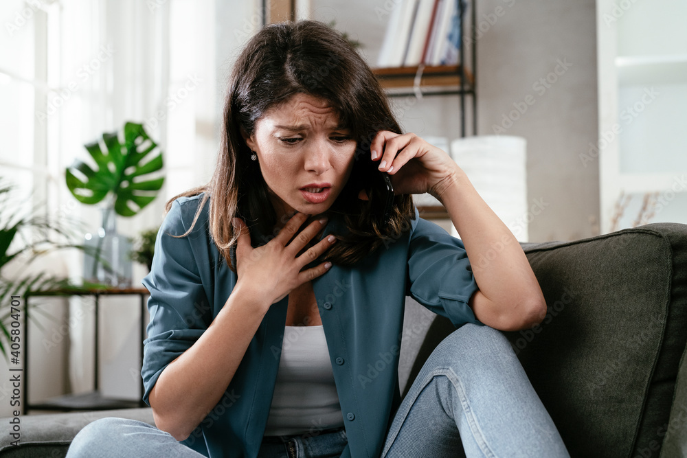 Sad woman sitting on the couch, using the phone. Upset woman talking to the phone. Sad woman sitting on the couch, using the phone. Upset woman talking to the phone.