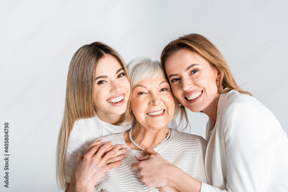 three generation of positive women smiling while looking at camera and hugging isolated on grey - obrazy, fototapety, plakaty 